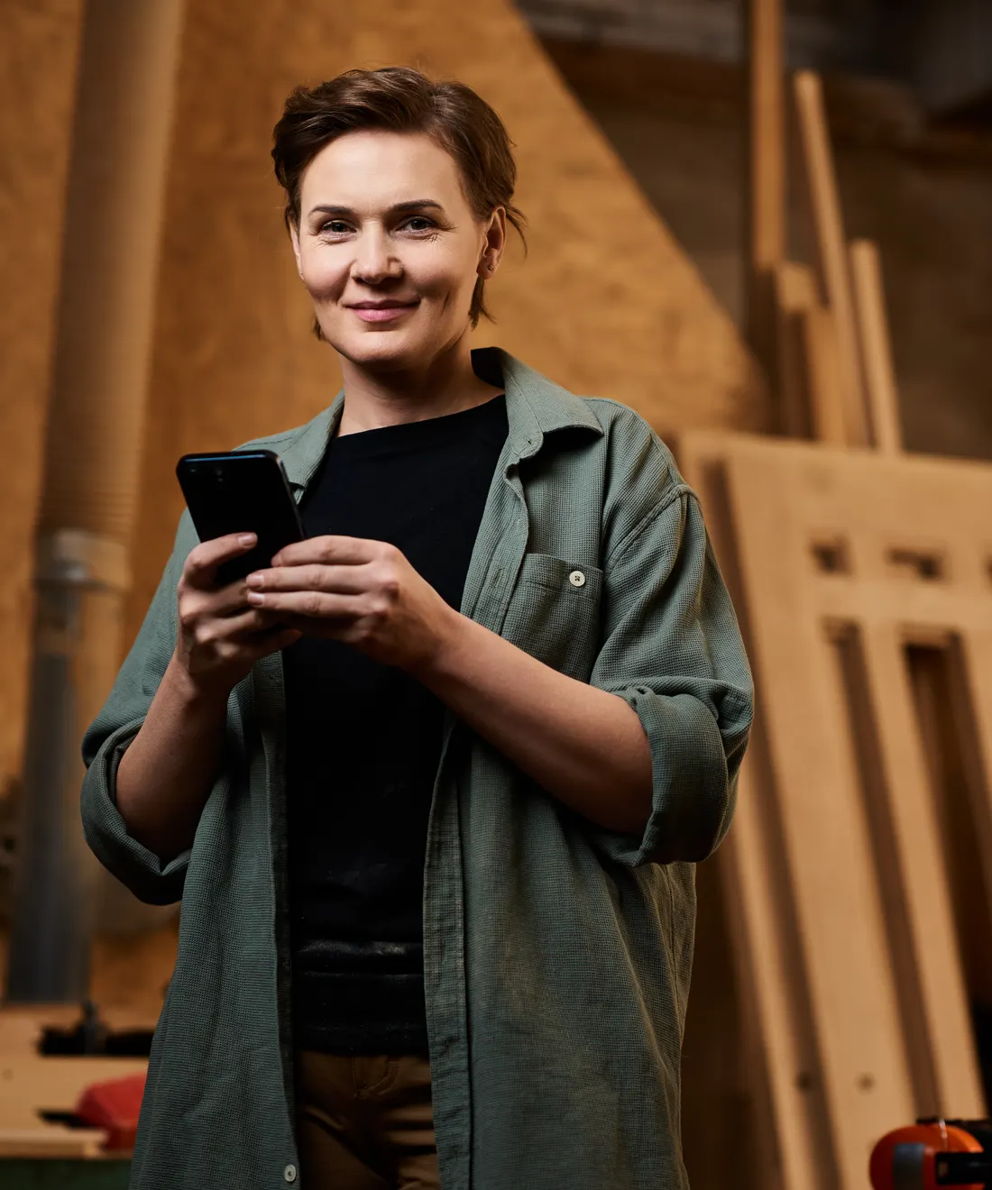 Truhlářka ve své dílně s radostí čte v mobilu novou poptávku z chatu